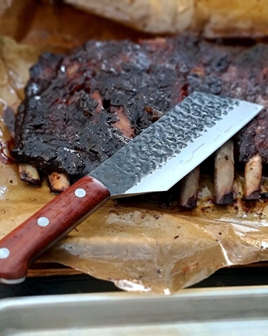 BBQ-kniv Kockkniv BBQmonster - robust kniv/cleaver med slida i läder. 5mm grov rygg och en vikt på 400 gram En bbq-kniv för BBQ och Grillning: BBQmonster BBQ-kniv / cleaver är kniven som är en kombination av en rejäl kockkniv och en Cleaver / köttyxa, och med denna i din hand är inte en kotlettrad eller ett revbensspjäll säkert någonstans. Bladet är EXTREMT stabilt och viker inte även vid hårdare tag. Ryggen är hela 5mm tjockt och större delen av bladet har en härlig hammrad yta som kniven rejält "intstagramvänlig" och photogenique. Denna BBQkniv kommer en slida av läder vilket gör att du kan bära den i din livrem eller i ditt förkläde. Skaftet är av polerat och lackat hårdträ och detta omsluter det genomgående knivbladet avslutning. Skaftet ger ett bra grepp och är enkelt att rengöra. Handtaget passar både höger- och vänsterhänta. Kolstål med blandning X50CrMoV15 Hårdhet 56° HRC vilket är ett relativt mjukt stål - något som gör att du själv enkelt kan hålla din kniv vass. Total längd: 29 cm Längd på bladet: 18 cm Längd på skaftet: 11 cm